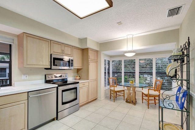 kitchen with a textured ceiling, stainless steel appliances, light brown cabinets, light tile patterned floors, and hanging light fixtures