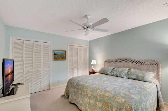 carpeted bedroom featuring a textured ceiling, ceiling fan, and two closets