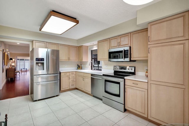 kitchen featuring sink, light brown cabinets, a textured ceiling, light tile patterned floors, and appliances with stainless steel finishes