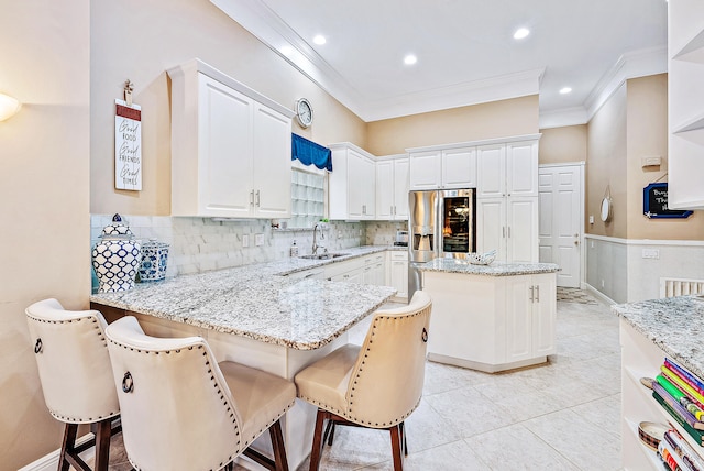 kitchen with kitchen peninsula, a kitchen breakfast bar, light stone counters, sink, and white cabinetry