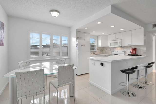 kitchen with tasteful backsplash, a textured ceiling, white appliances, white cabinetry, and light tile patterned flooring