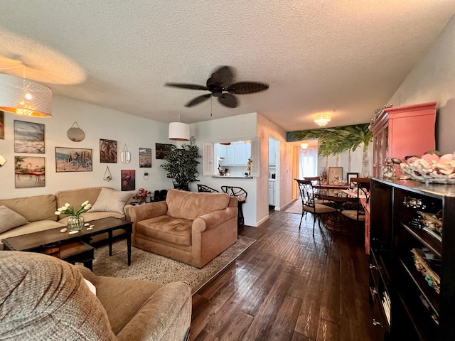 living room with a textured ceiling, ceiling fan, and dark wood-type flooring