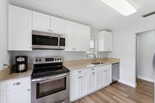 kitchen with sink, white cabinets, light hardwood / wood-style flooring, and appliances with stainless steel finishes