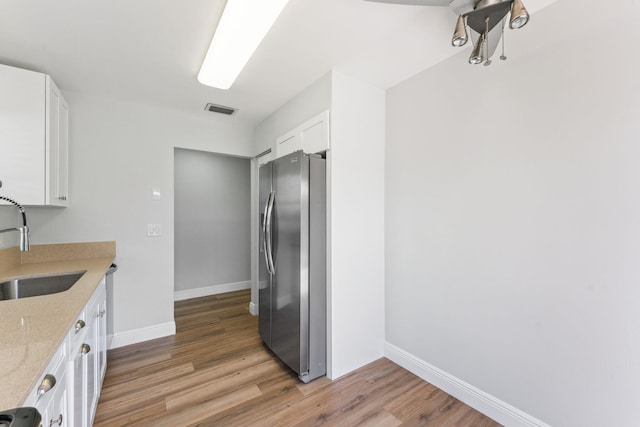 kitchen with white cabinetry, stainless steel fridge, wood-type flooring, and light stone counters