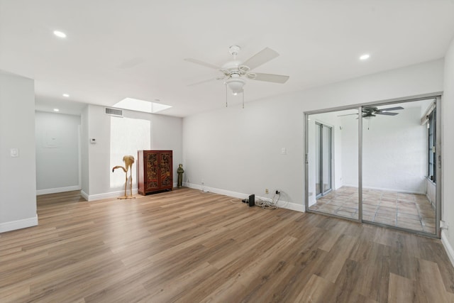 unfurnished living room featuring wood-type flooring, a skylight, and ceiling fan