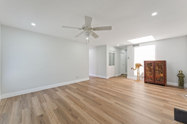 unfurnished living room with ceiling fan, a skylight, and light hardwood / wood-style flooring