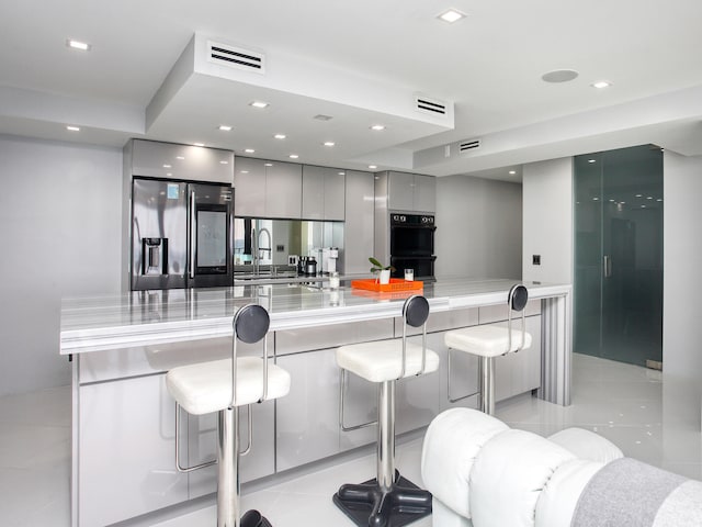 kitchen with fridge with ice dispenser, sink, double oven, gray cabinets, and a breakfast bar