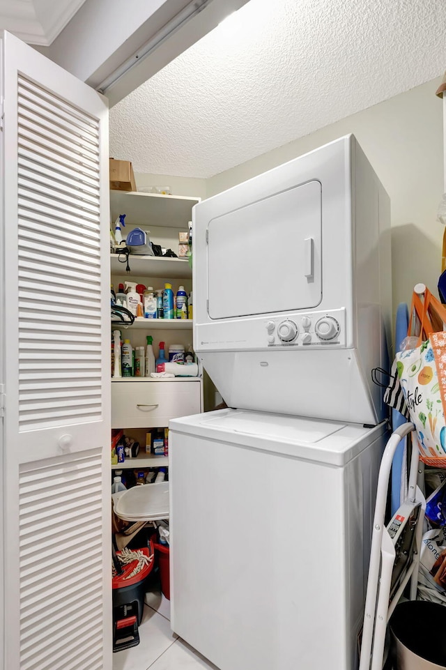 laundry area with light tile patterned floors, stacked washing maching and dryer, and a textured ceiling