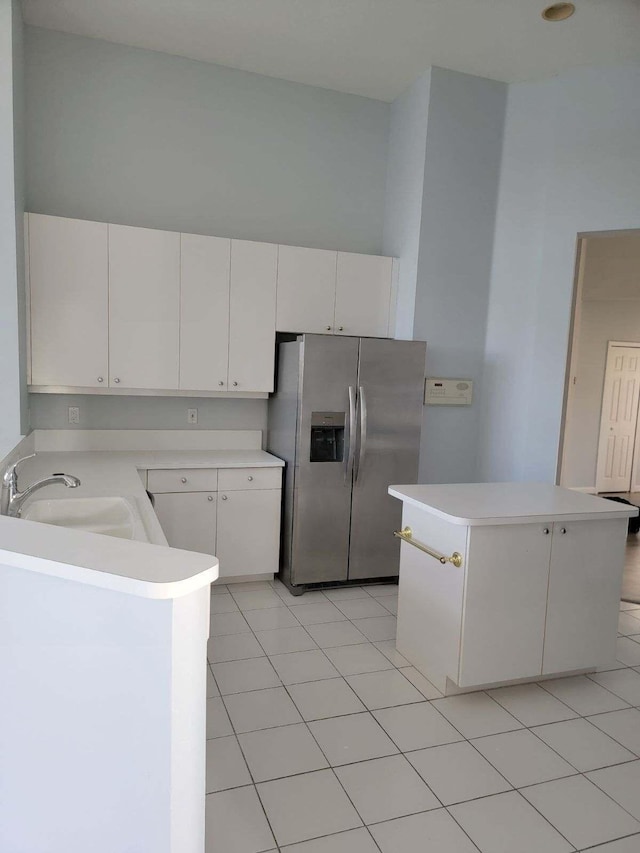 kitchen with a center island, sink, stainless steel refrigerator with ice dispenser, light tile patterned floors, and white cabinetry