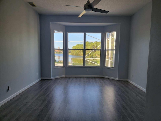 unfurnished room with a textured ceiling, dark hardwood / wood-style floors, ceiling fan, and a water view