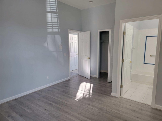 unfurnished bedroom with ensuite bathroom, light wood-type flooring, a towering ceiling, and a closet