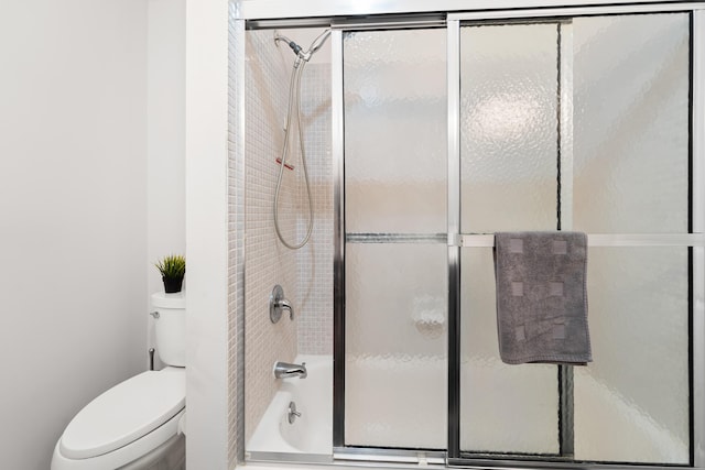 bathroom featuring toilet and bath / shower combo with glass door