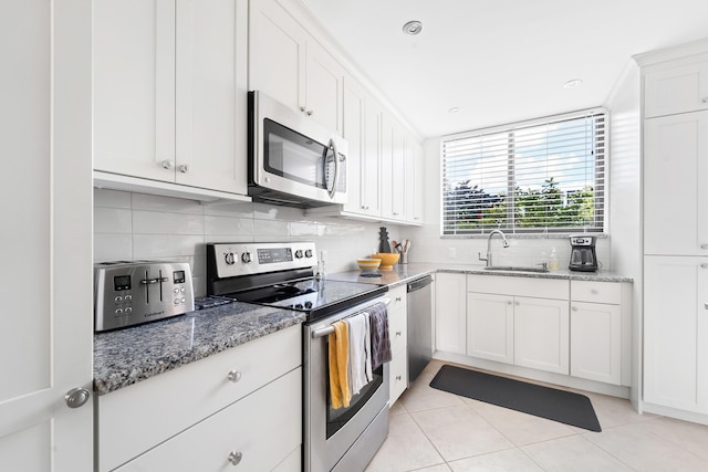 kitchen featuring light stone countertops, white cabinetry, sink, stainless steel appliances, and light tile patterned floors