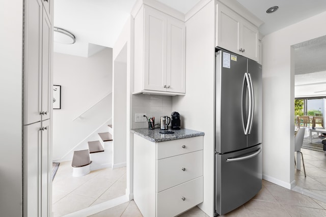 kitchen with stainless steel refrigerator, white cabinetry, light stone countertops, and decorative backsplash