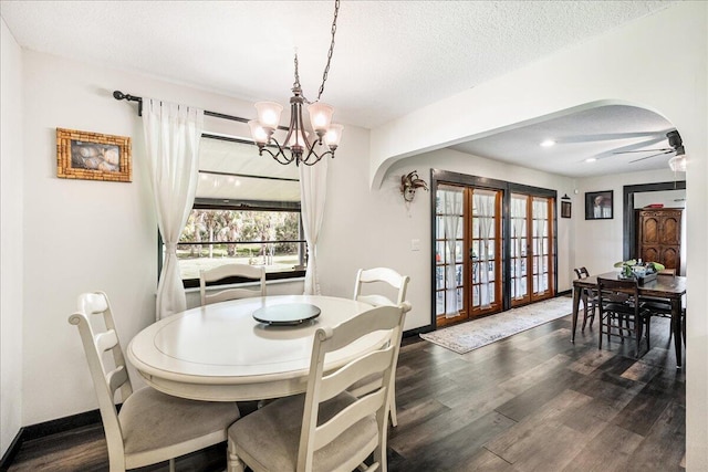 dining area with a textured ceiling, ceiling fan with notable chandelier, french doors, and dark wood-type flooring