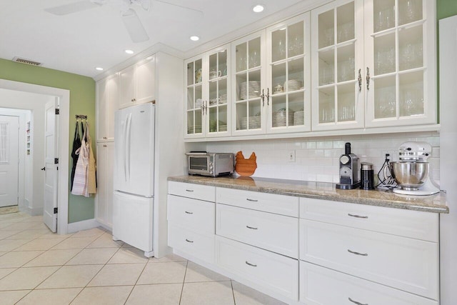 kitchen featuring decorative backsplash, light stone counters, light tile patterned floors, white fridge, and white cabinetry