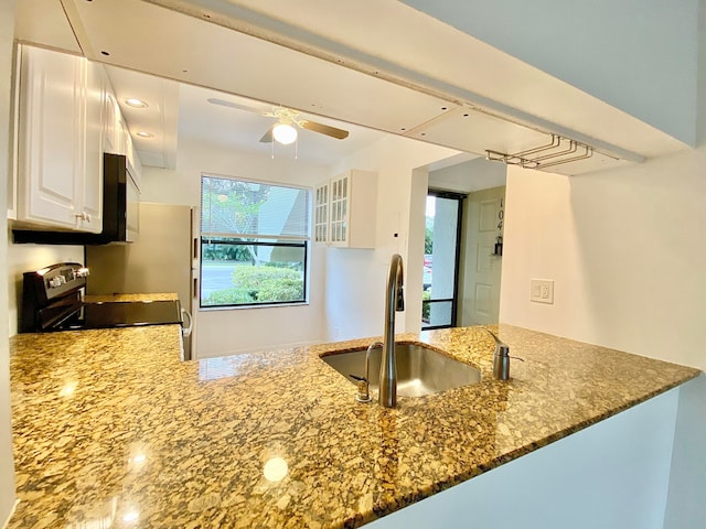 kitchen with stone counters, range, kitchen peninsula, ceiling fan, and white cabinetry