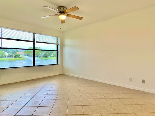 empty room with a water view, ceiling fan, and light tile patterned floors