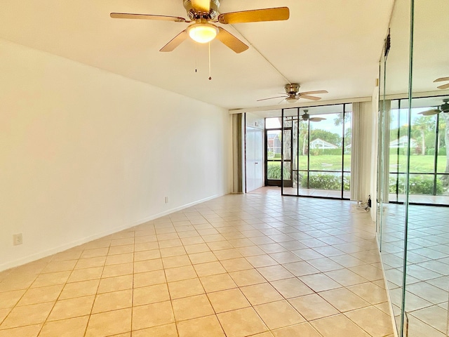 spare room featuring ceiling fan, expansive windows, and light tile patterned floors