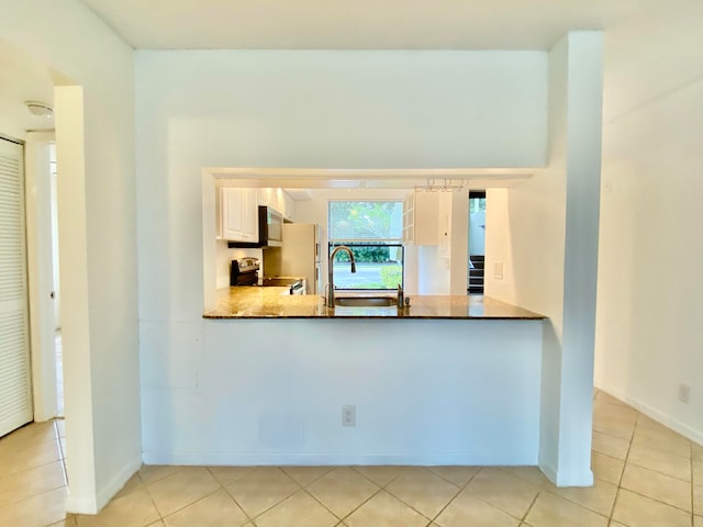 kitchen with kitchen peninsula, appliances with stainless steel finishes, sink, light tile patterned floors, and white cabinets