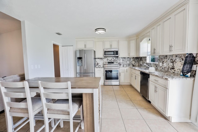 kitchen with sink, decorative backsplash, light tile patterned floors, light stone counters, and stainless steel appliances