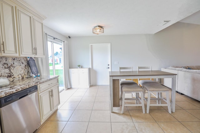 kitchen with stainless steel dishwasher, light tile patterned floors, light stone countertops, and cream cabinetry