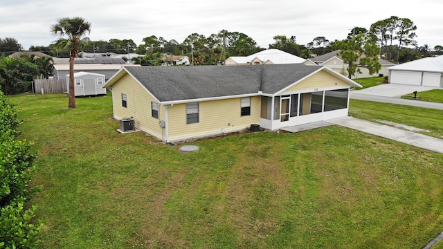 rear view of property featuring a sunroom, a storage shed, a yard, and central air condition unit