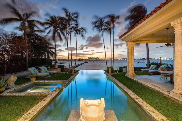 pool at dusk with a patio area, an in ground hot tub, a water view, and ceiling fan