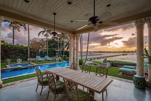 patio terrace at dusk with ceiling fan, a swimming pool with hot tub, and a water view