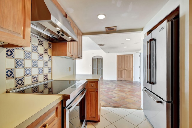 kitchen featuring kitchen peninsula, appliances with stainless steel finishes, light tile patterned floors, and wall chimney range hood