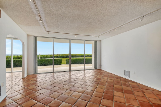 unfurnished room featuring light tile patterned flooring, a wall of windows, a textured ceiling, and track lighting