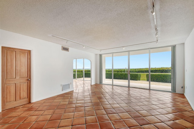 tiled spare room featuring a textured ceiling, track lighting, and a wall of windows