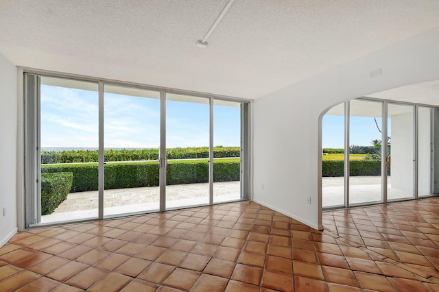 tiled empty room featuring a textured ceiling and a wall of windows