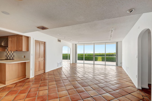 unfurnished living room with a textured ceiling, floor to ceiling windows, light tile patterned flooring, and rail lighting