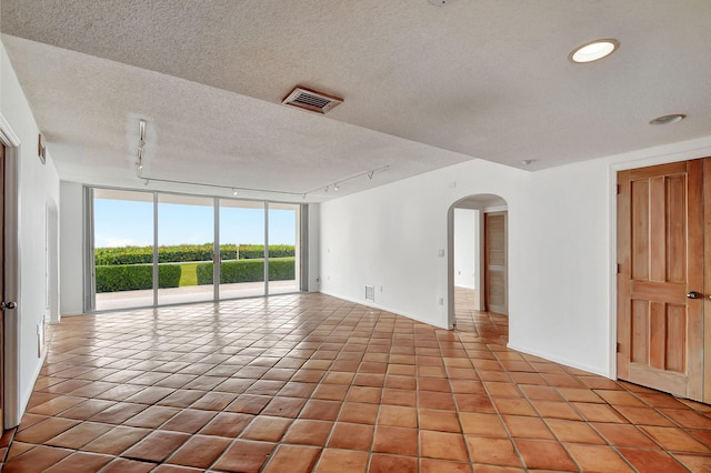 tiled empty room featuring a textured ceiling, rail lighting, and floor to ceiling windows