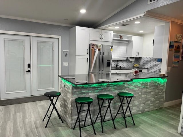 kitchen featuring kitchen peninsula, stainless steel refrigerator with ice dispenser, white cabinetry, and ornamental molding