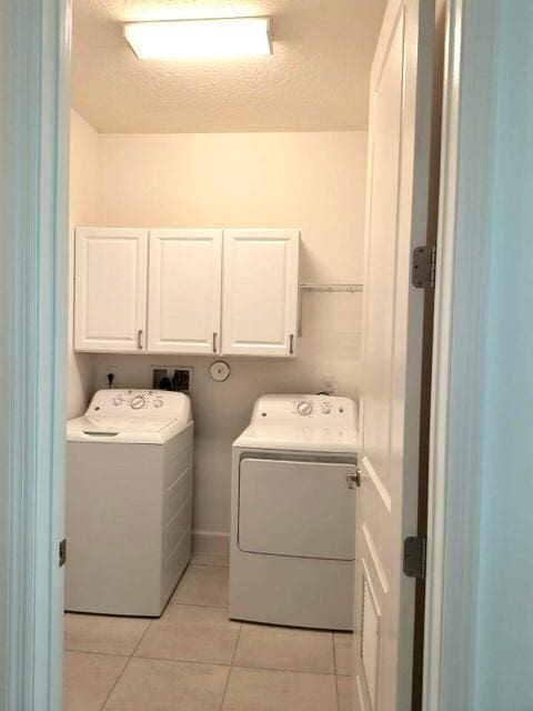 washroom featuring cabinets, light tile patterned floors, a textured ceiling, and washing machine and clothes dryer