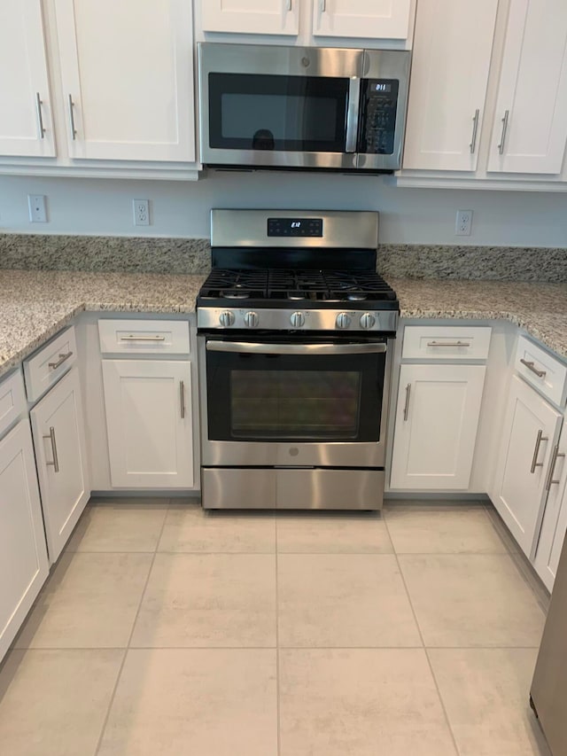 kitchen featuring white cabinetry, light tile patterned floors, light stone countertops, and appliances with stainless steel finishes