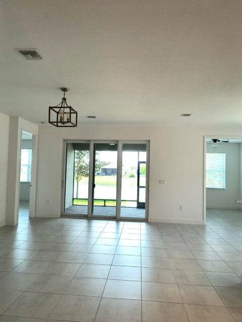 unfurnished room featuring light tile patterned floors, ceiling fan with notable chandelier, a textured ceiling, and a healthy amount of sunlight