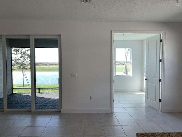 spare room with a water view, light tile patterned floors, and a textured ceiling