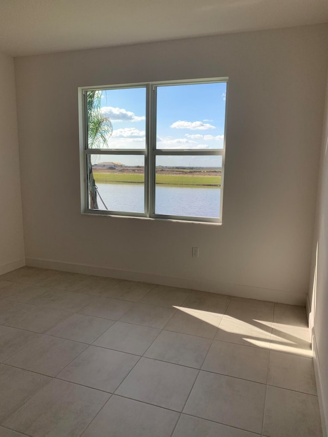 spare room with a water view, a healthy amount of sunlight, and light tile patterned floors