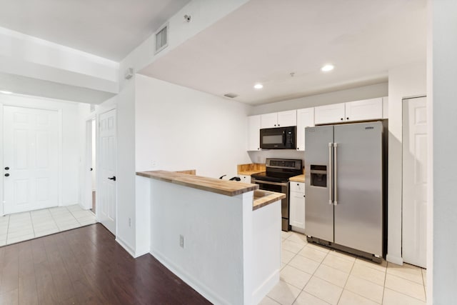 kitchen with appliances with stainless steel finishes, wood counters, white cabinets, light tile patterned floors, and kitchen peninsula