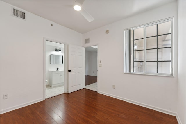 unfurnished bedroom featuring multiple windows, connected bathroom, hardwood / wood-style flooring, and sink