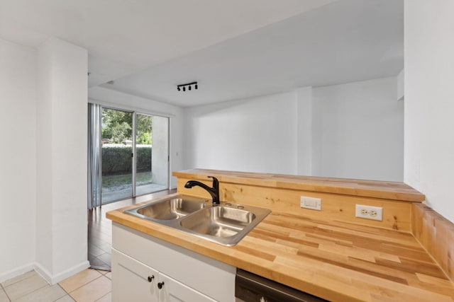 kitchen with sink, light tile patterned floors, wooden counters, dishwasher, and white cabinetry