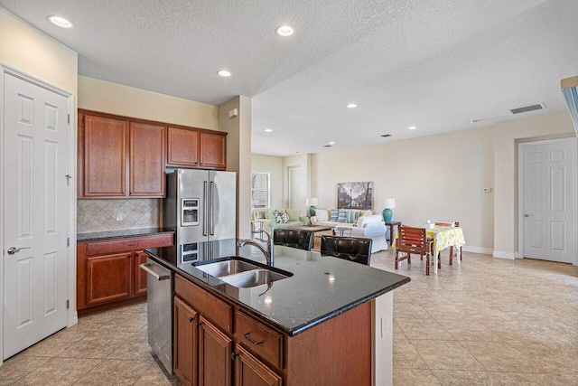 kitchen featuring tasteful backsplash, a center island with sink, sink, appliances with stainless steel finishes, and a textured ceiling