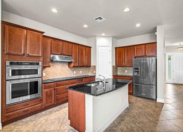 kitchen with tasteful backsplash, sink, a kitchen island with sink, stainless steel appliances, and dark stone counters