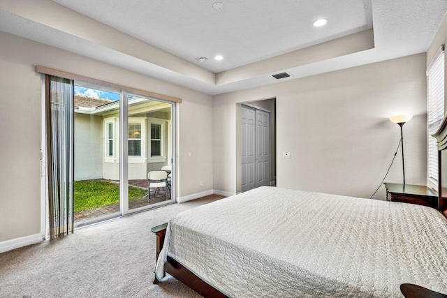 bedroom with access to exterior, a tray ceiling, a closet, and carpet flooring