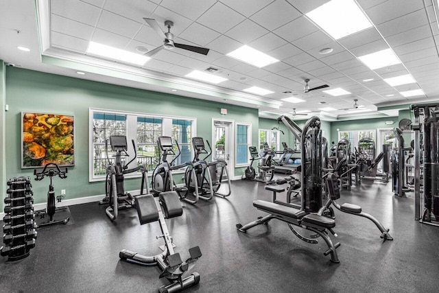 workout area with a paneled ceiling, ceiling fan, visible vents, and baseboards