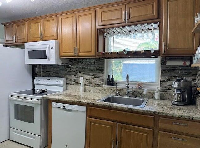 kitchen with backsplash, light stone counters, white appliances, and sink