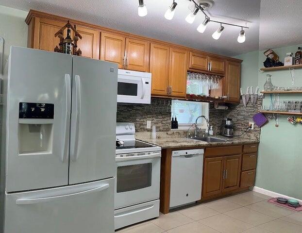 kitchen featuring decorative backsplash, light tile patterned floors, white appliances, and sink